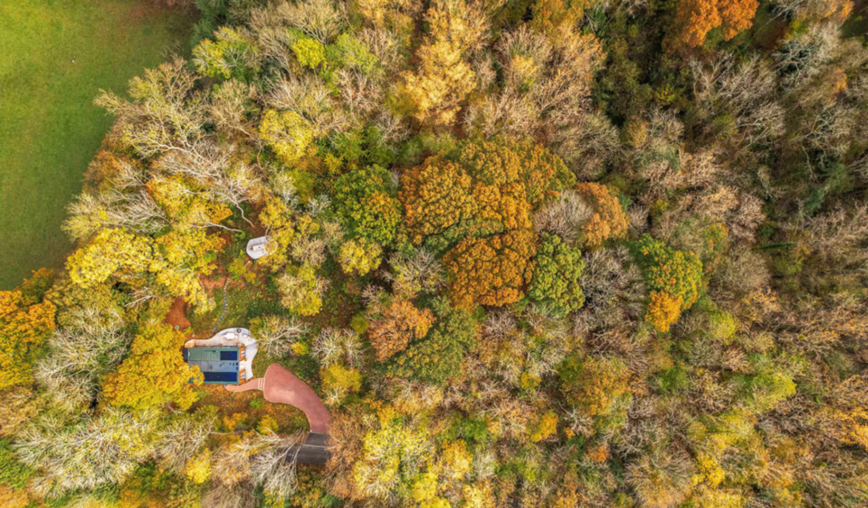 Aerial view of a sustainable property nestled among autumn woodland and green meadow